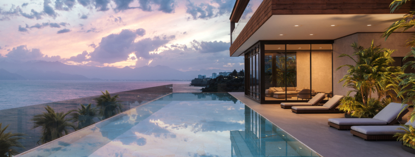 Infinity pool by a modern house, crafted by a top pool contractor, overlooks the ocean at sunset. Lounge chairs and tropical plants line the deck as pastel clouds reflect on calm water for a serene escape.